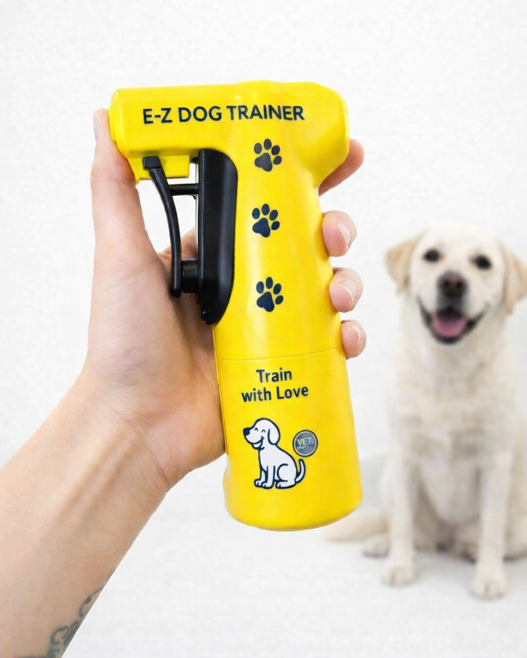 ellow E-Z Dog Trainer device held by a person with a dog in the background.